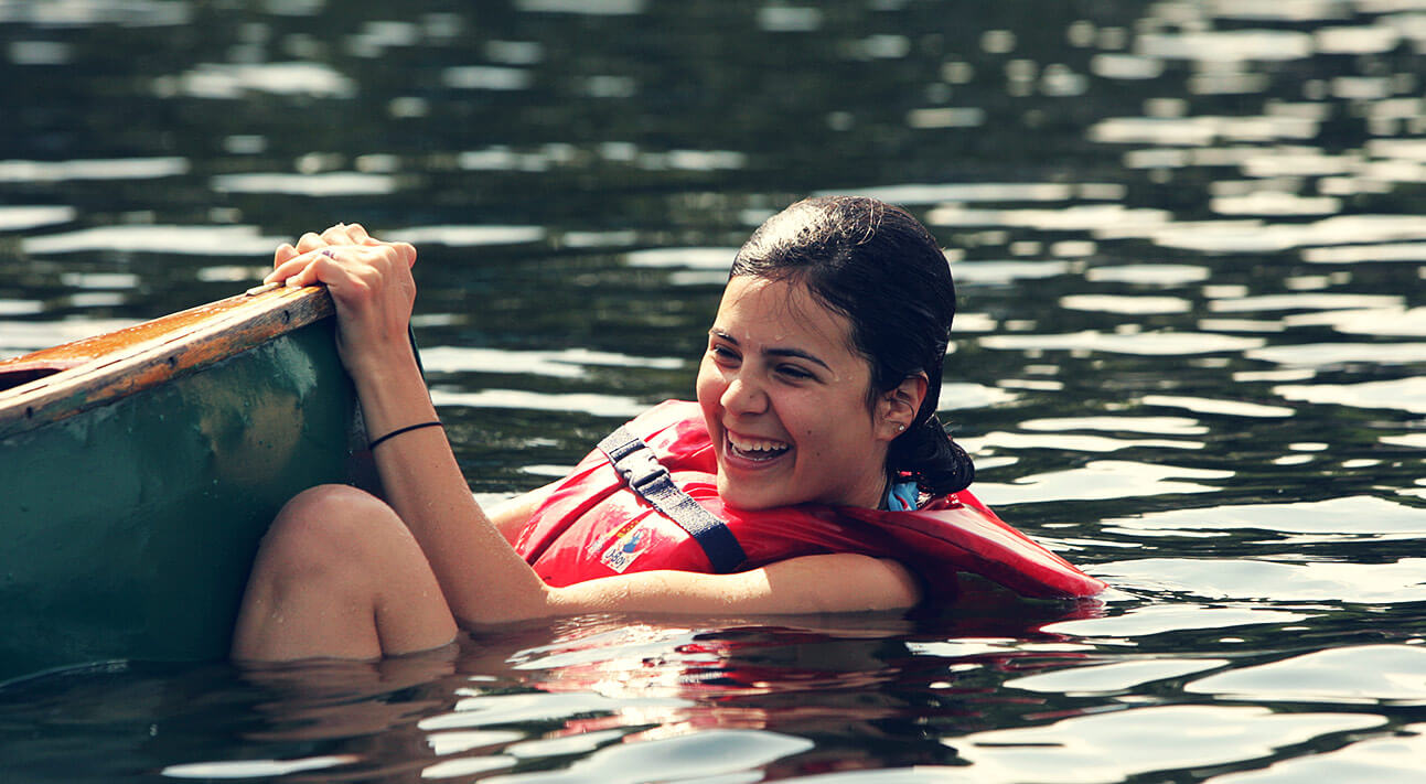 A girl enjoying herself in the pond hanging off the end of a boat.