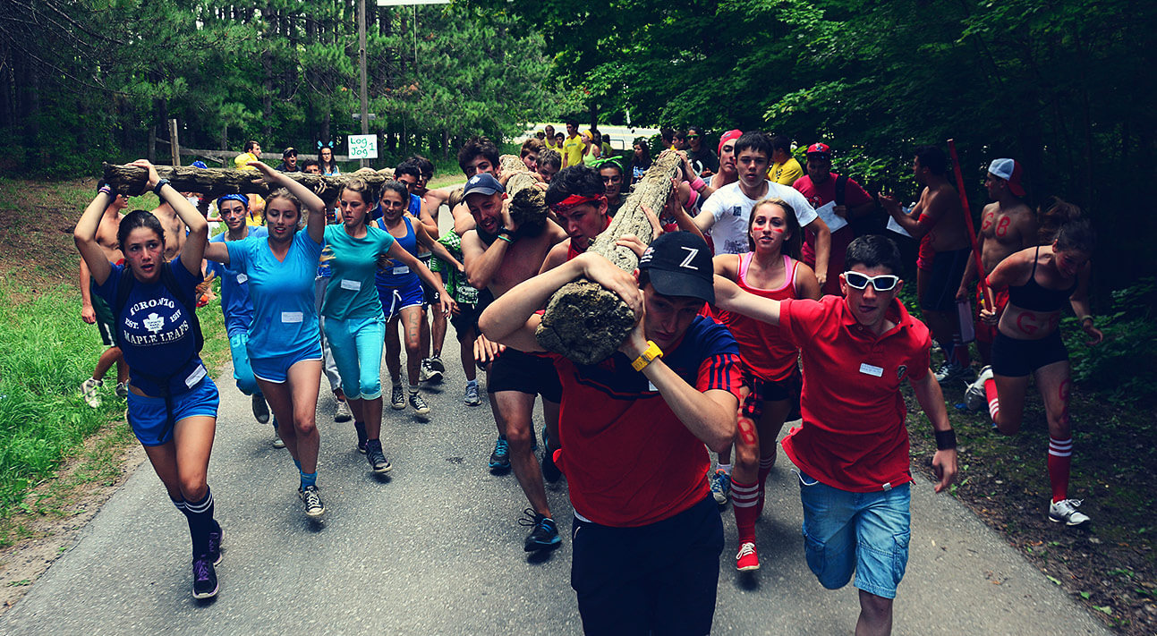 A group of older campers hauling large logs overhead